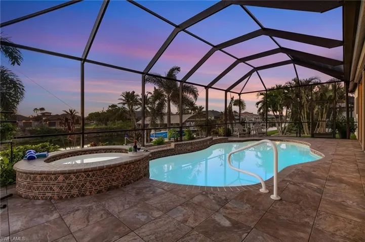 Pool at dusk with a patio, a lanai, and an in ground hot tub
