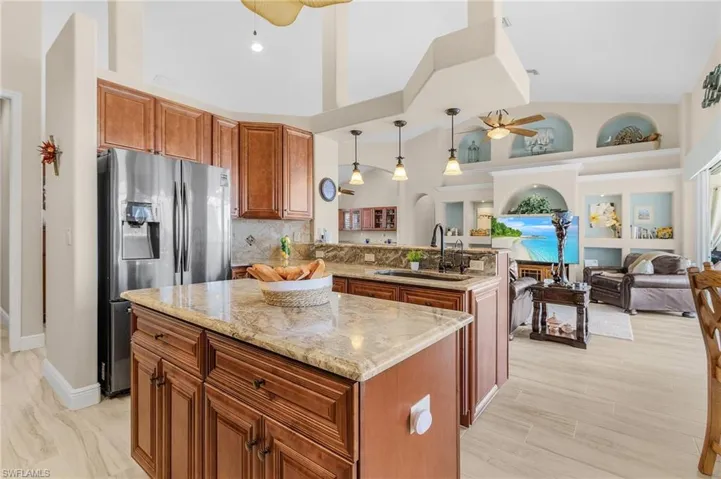 Kitchen featuring light stone countertops, stainless steel refrigerator with ice dispenser, sink, pendant lighting, and a kitchen island