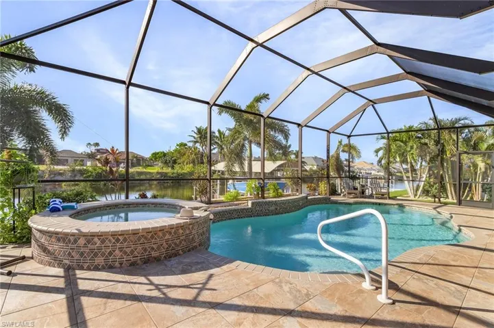View of swimming pool featuring glass enclosure, a patio area, a water view, and an in ground hot tub