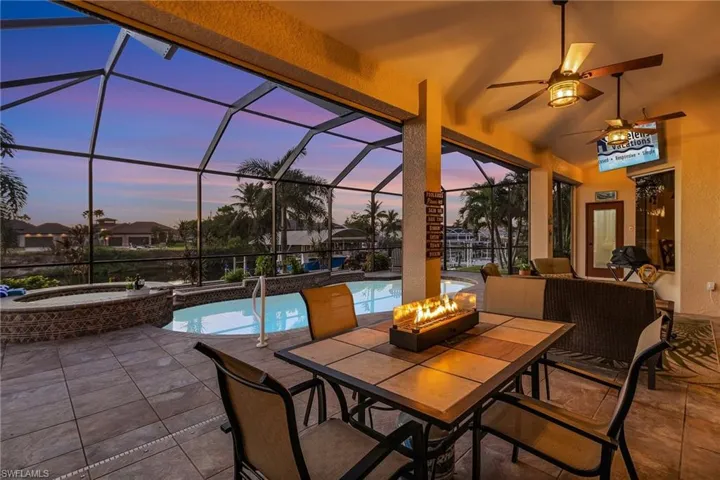 Patio terrace at dusk with glass enclosure, a swimming pool with hot tub, an outdoor fire pit, and ceiling fan