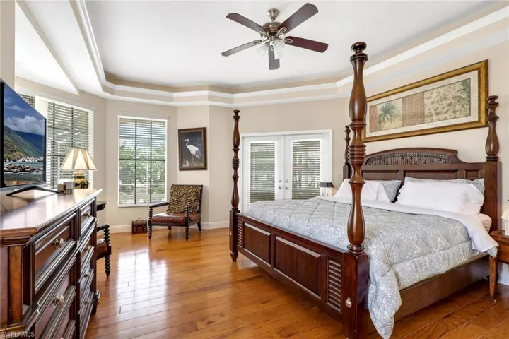Bay window with multiple windows, wood-finish flooring, tray ceiling, ceiling fan, and double doors with integrated blinds