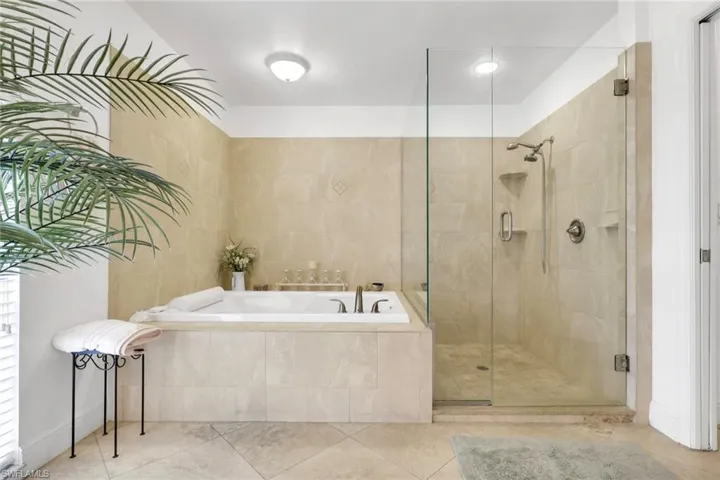 Spa-inspired bathroom featuring a built-in soaking tub, a glass-enclosed shower, tiled walls, and tiled flooring