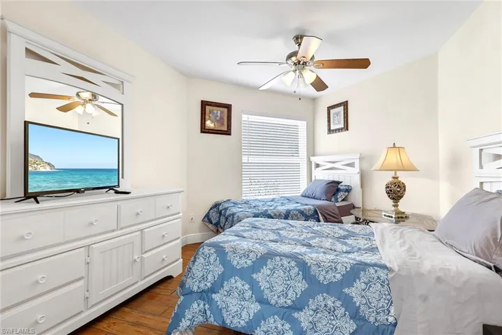 Room featuring two beds, wood-finish flooring, and a ceiling fan with light fixture