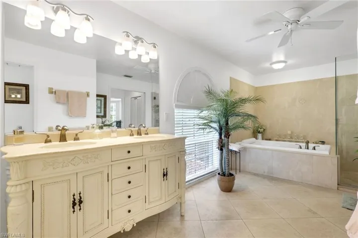 Spacious bathroom featuring a double vanity with an ornate base and integrated sinks, a large soaking tub, and a separate glass-enclosed shower
