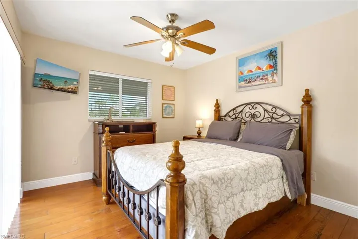 Wood-finish flooring accentuates this bedroom featuring a ceiling fan, window with blinds, and light-colored walls