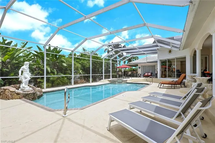 Screened-in pool area featuring a rectangular pool, integrated spa, and expansive paved deck