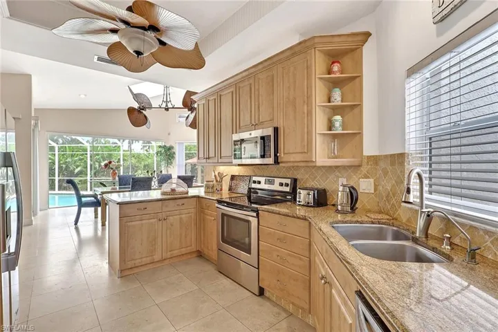 Kitchen featuring light wood cabinetry, stainless steel appliances, a double basin sink, stone countertops, and a tiled backsplash