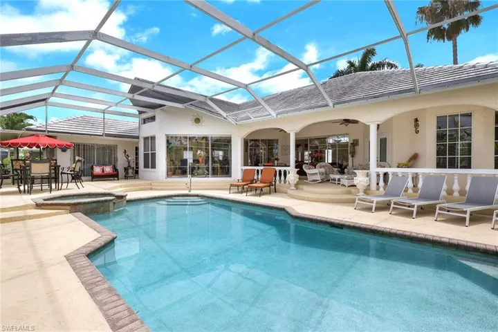 Screened-in outdoor living space featuring a blue-tiled swimming pool and integrated spa