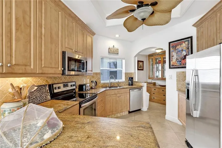 Kitchen featuring light wood cabinetry, granite countertops, stainless steel appliances, a tiled backsplash, and a ceiling fan