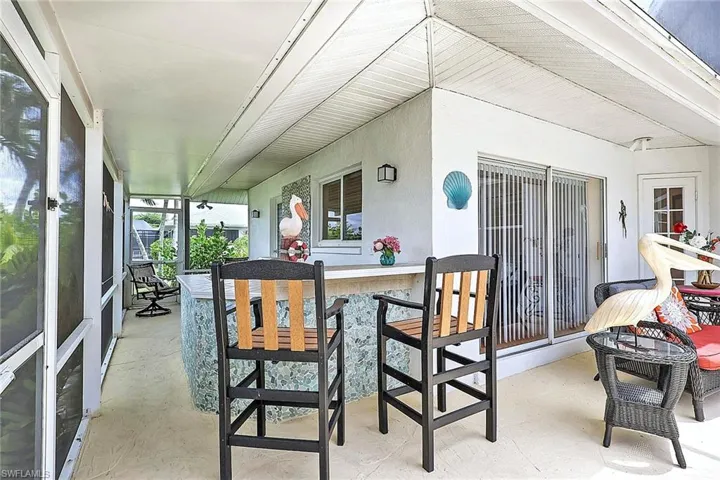 Screened lanai featuring a built-in bar with a stone-finish facade, an overhead ceiling fan, and sliding glass door access