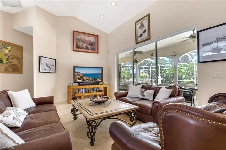 Living area featuring vaulted ceilings, recessed lighting, tile flooring, and large sliding glass doors opening to a screened outdoor space