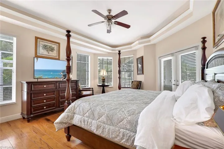 Warm bedroom featuring wood-finish flooring, a tray ceiling, and multiple windows with horizontal blinds