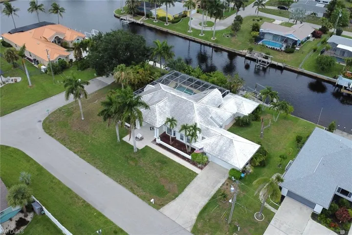 Waterfront property featuring a screened-in pool enclosure, mature palm trees, a concrete driveway, and a boat dock on the canal