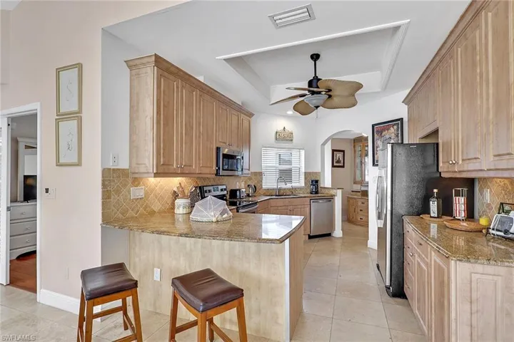 Kitchen featuring light wood cabinetry, granite countertops, stainless steel appliances, and a tiled backsplash