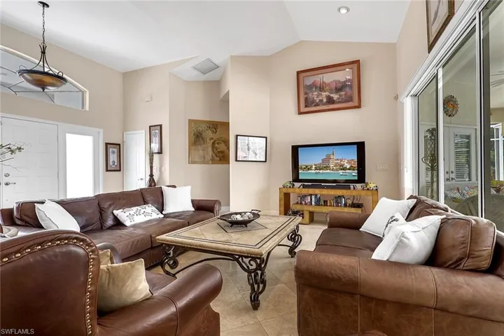 Spacious living area featuring vaulted ceilings, tile flooring, and large sliding glass doors providing abundant natural light