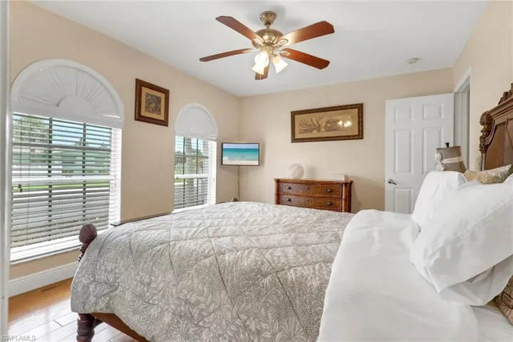 Room featuring two arched windows with blinds, wood-finish flooring, and a ceiling fan with integrated lighting