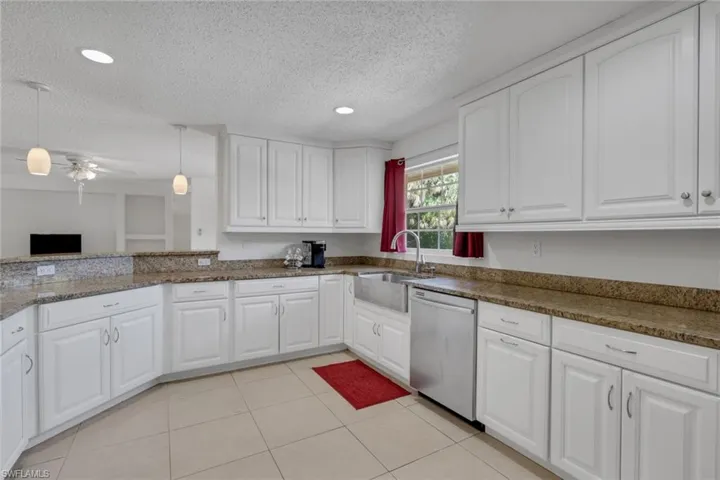 Kitchen with white cabinets, dishwasher, hanging light fixtures, light tile patterned floors, and a textured ceiling
