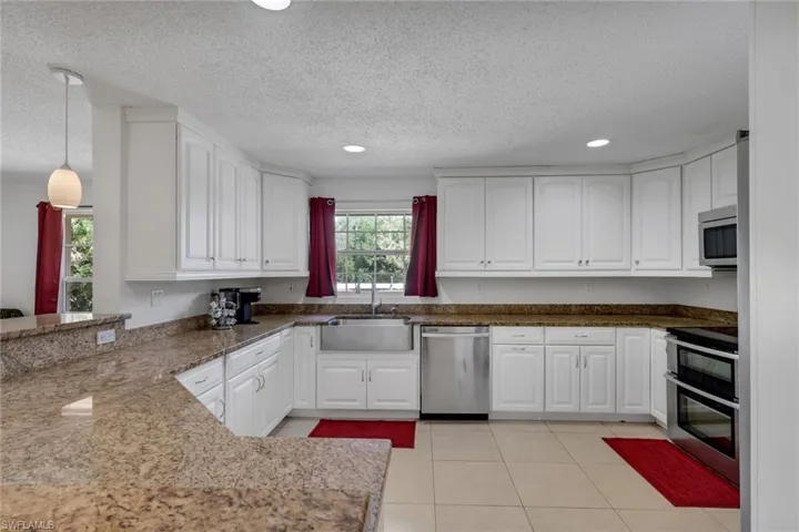 Kitchen featuring white cabinets, stainless steel appliances, dark stone countertops, light tile patterned floors, and a textured ceiling