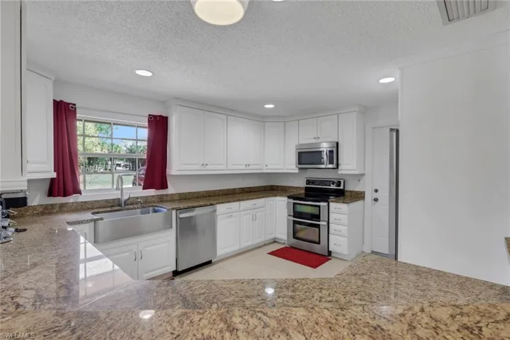 Kitchen with stainless steel appliances, recessed lighting, white cabinets, a textured ceiling, and dark stone countertops