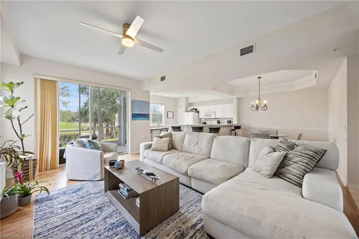 Living room featuring light hardwood / wood-style flooring, ceiling fan with notable chandelier, and a raised ceiling