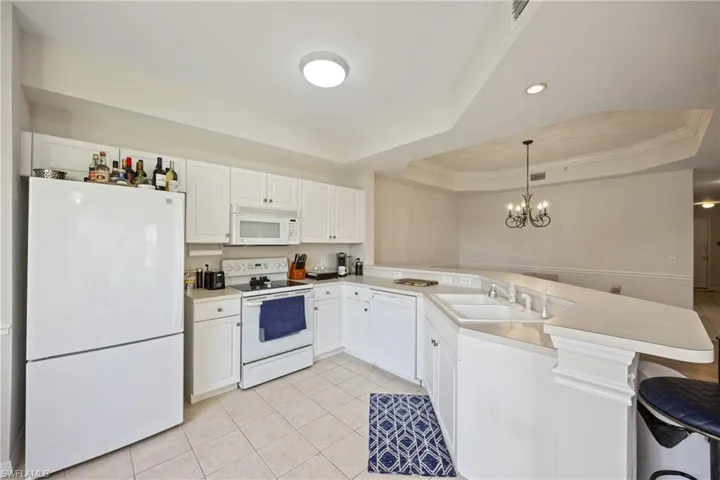 Kitchen with kitchen peninsula, a tray ceiling, pendant lighting, white cabinets, and white appliances
