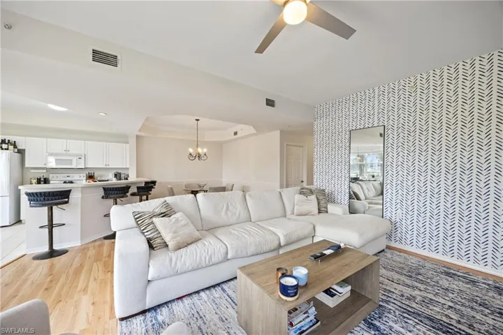 Living room featuring light hardwood / wood-style floors, a raised ceiling, and ceiling fan with notable chandelier