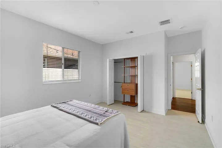 Smartly organized space featuring light vinyl plank floors, custom closet built-ins, clean white panel doors, and horizontal window blinds.