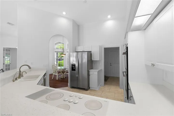 Kitchen featuring white cabinetry, stainless steel refrigerator, integrated cooktop, undermount sink with gooseneck faucet and recessed lighting