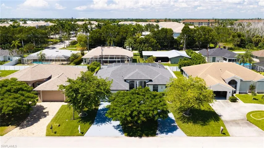 Residential property with a gray shingle roof, mature landscaping, and a paved driveway