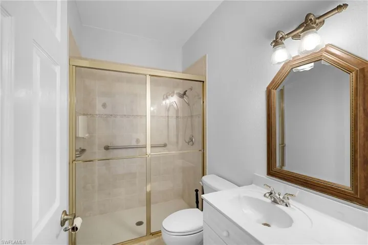Sleek tiled shower with glass enclosure, single white vanity, and an ornate statement mirror lit by bright overhead fixtures.