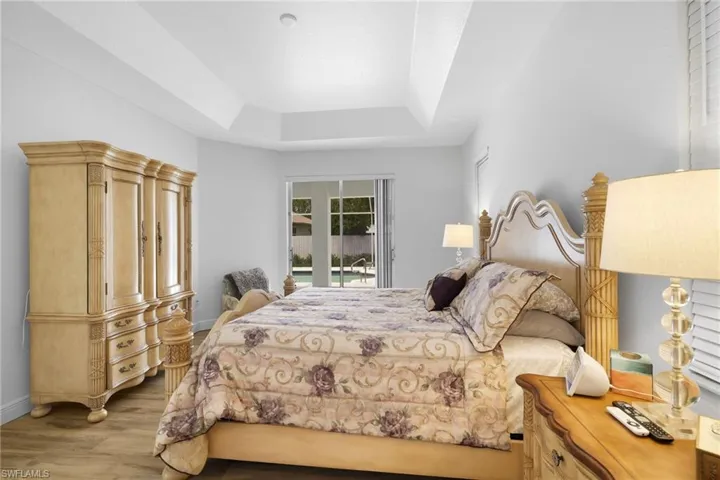 Primary Bedroom with tray ceiling, vinyl flooring, sliding glass door leading to the pool.