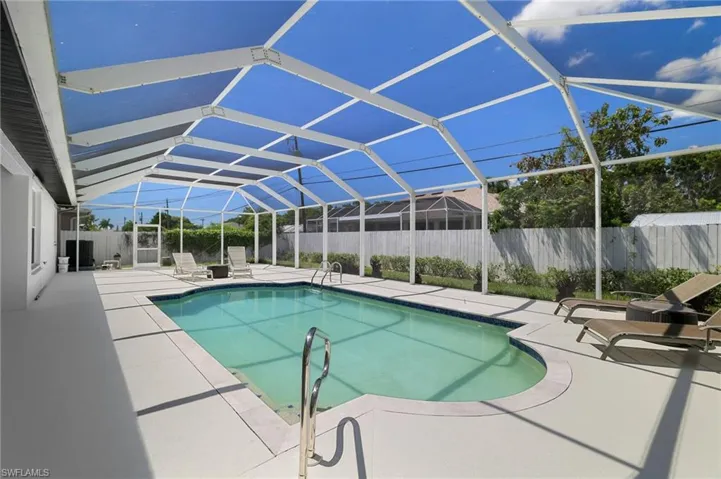 Sunlit screened pool retreat framed by a clean concrete deck, serene mature landscaping, and classic white fencing.
