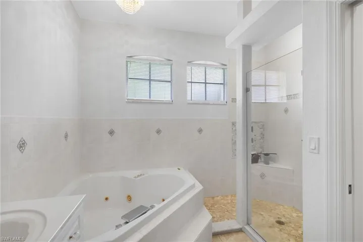 Corner jetted soaking tub, glass-enclosed shower with tiled bench and dual arched windows.