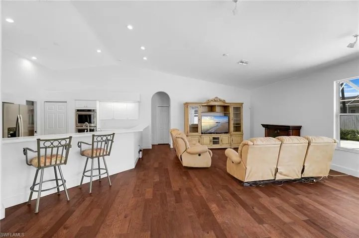 Vaulted ceilings with recessed lighting, wood flooring, white kitchen cabinetry with stainless steel appliances and a kitchen island with a breakfast bar.