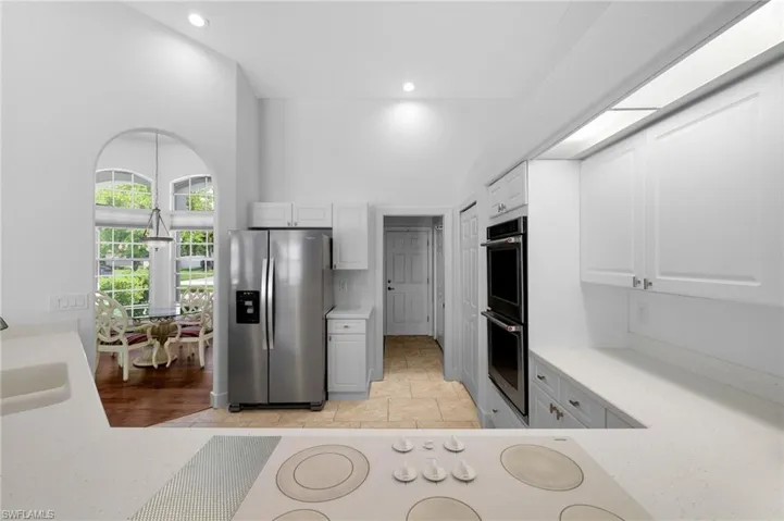 Modern kitchen featuring stainless steel refrigerator with ice and water dispenser, dual wall ovens with black glass fronts, white cabinetry, ceramic cooktop and arched transom window.