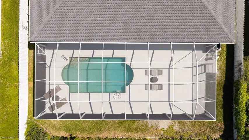 Screened-in pool enclosure featuring a kidney-shaped pool, extensive paved decking, and a gray shingle roofline