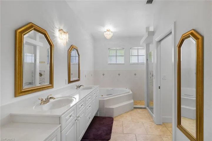 Dual vanity with undermount sinks, jetted tub, walk-in shower with glass enclosure and tiled flooring.
