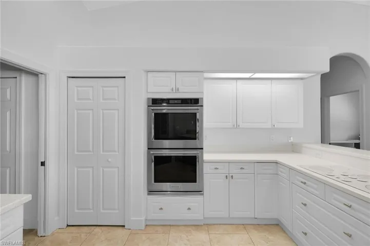 White cabinetry with brushed nickel hardware, built-in double ovens, light-toned countertops, and tile flooring