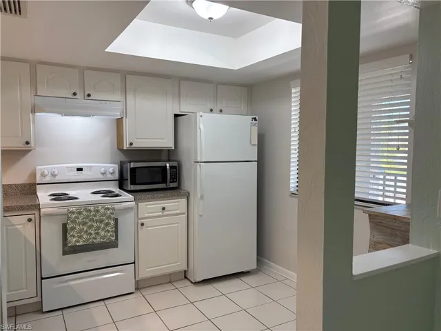 Kitchen featuring white appliances, light tile patterned floors, and white cabinetry