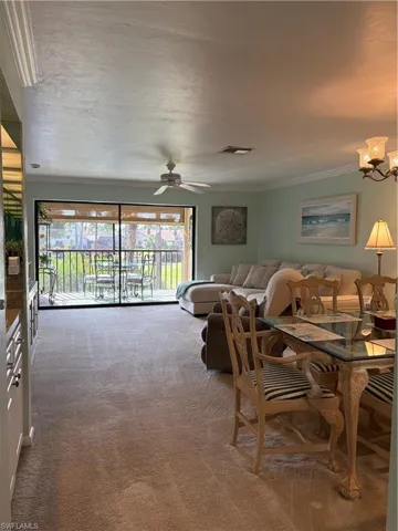 Living area featuring light colored carpet, a ceiling fan, ornamental molding, and a chandelier