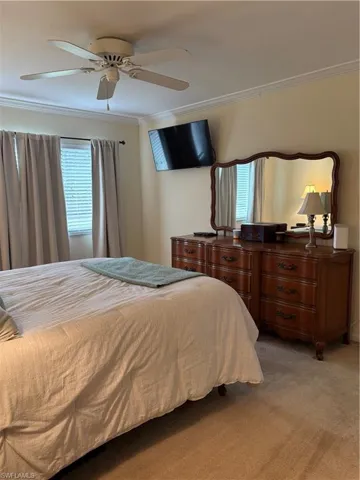 Bedroom with a ceiling fan, crown molding, and light colored carpet