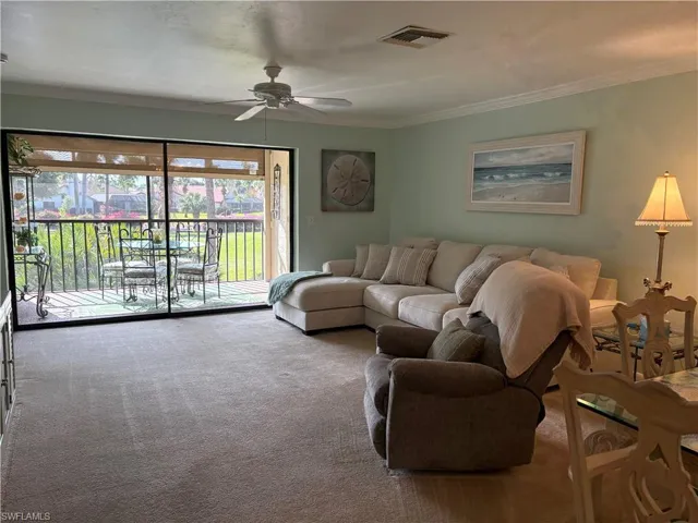 Carpeted living room with a ceiling fan and ornamental molding