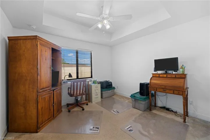 Office with a tray ceiling, light carpet, baseboards, and ceiling fan