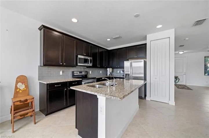 Kitchen featuring tasteful backsplash, light stone countertops, light tile patterned floors, stainless steel appliances, and a sink
