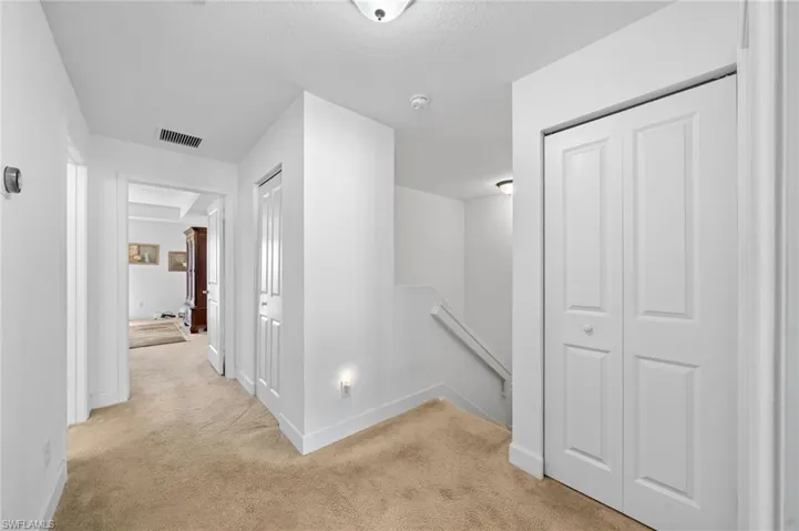 Hallway featuring baseboards, visible vents, an upstairs landing, and carpet floors