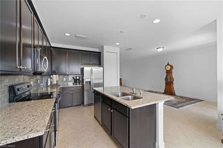 Kitchen with a kitchen island with sink, a sink, backsplash, appliances with stainless steel finishes, and light tile patterned floors