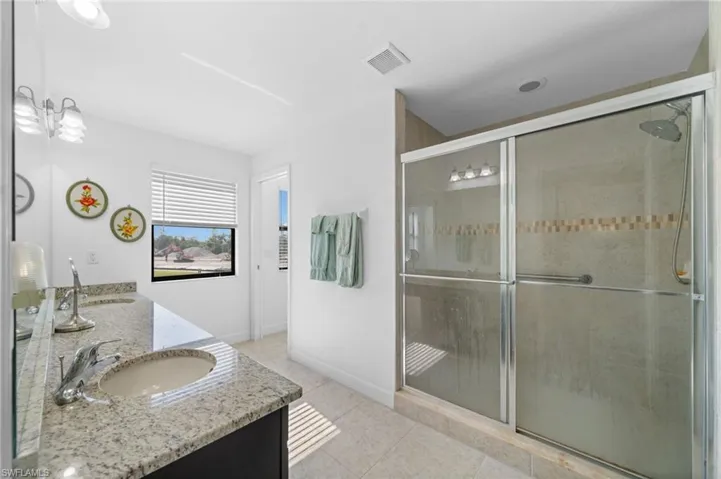 Bathroom with visible vents, double vanity, a stall shower, tile patterned floors, and a sink