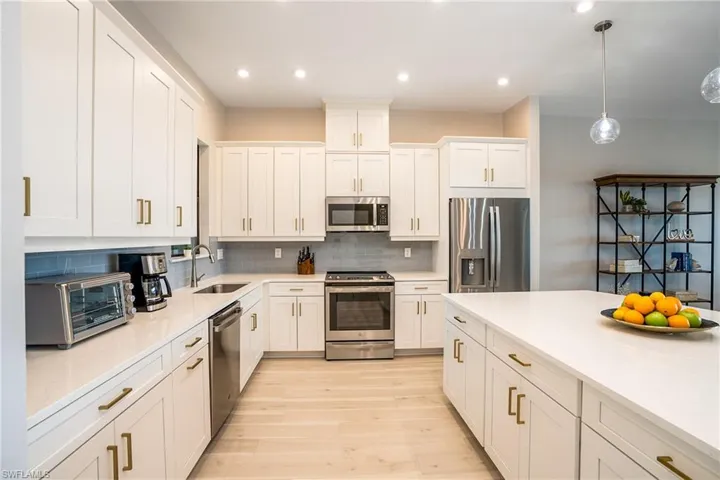 Kitchen featuring appliances with stainless steel finishes, light wood finished floors, white cabinetry, tasteful backsplash, and light countertops