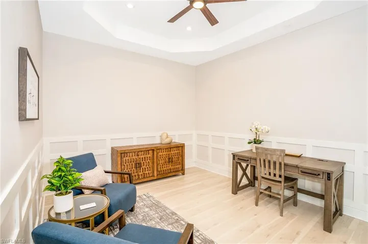 Living area featuring a decorative wall, a tray ceiling, ceiling fan, light wood-style flooring, and a wainscoted wall