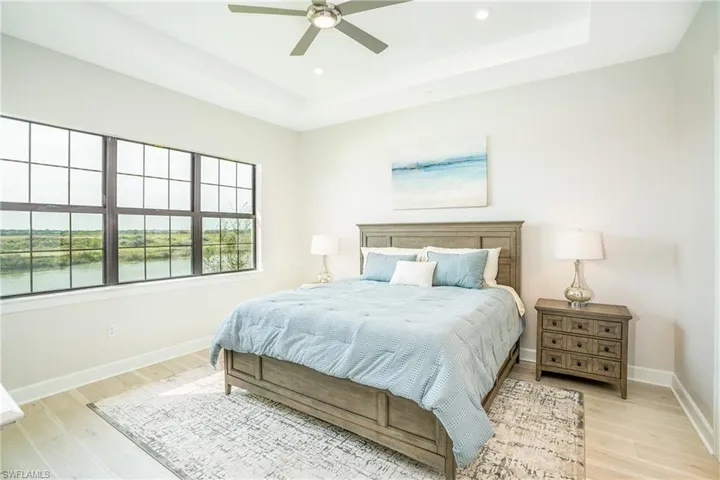 Bedroom with a raised ceiling, light wood-style floors, recessed lighting, and a ceiling fan